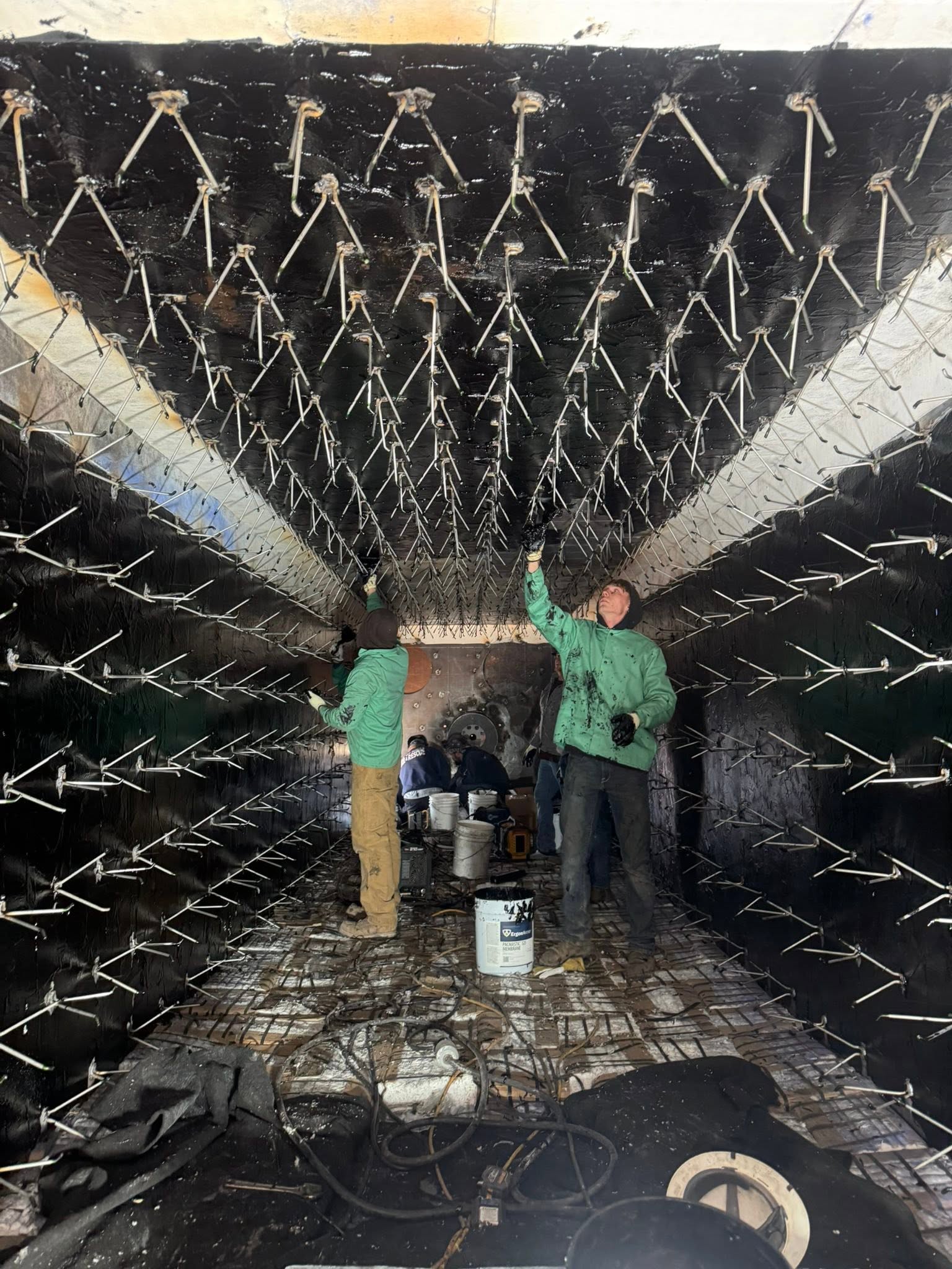 Two crew members coating the anchor grid inside a refractory-lined duct